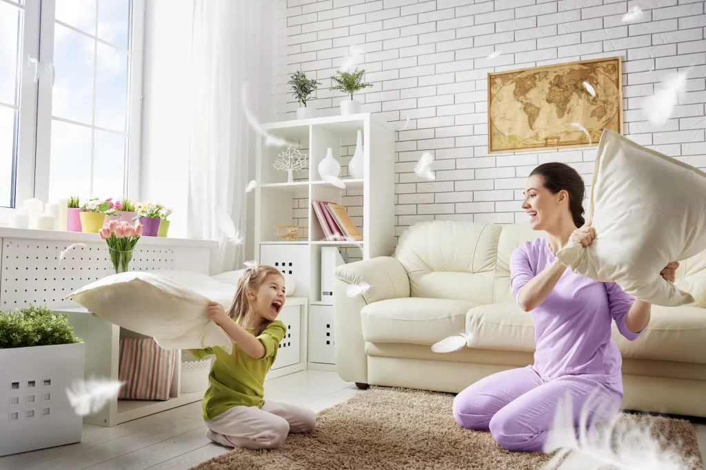 Perks of being a babysitter Babysitter playing with pillows in the living room with mother and daughter.
