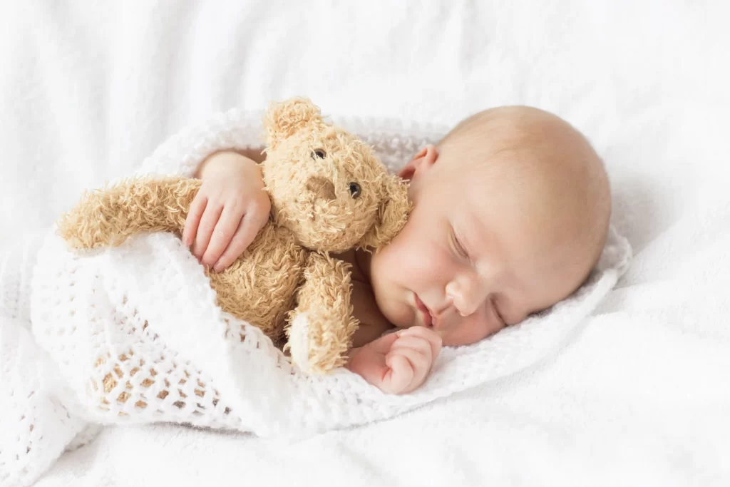 A peaceful newborn baby snuggles with a teddy bear.