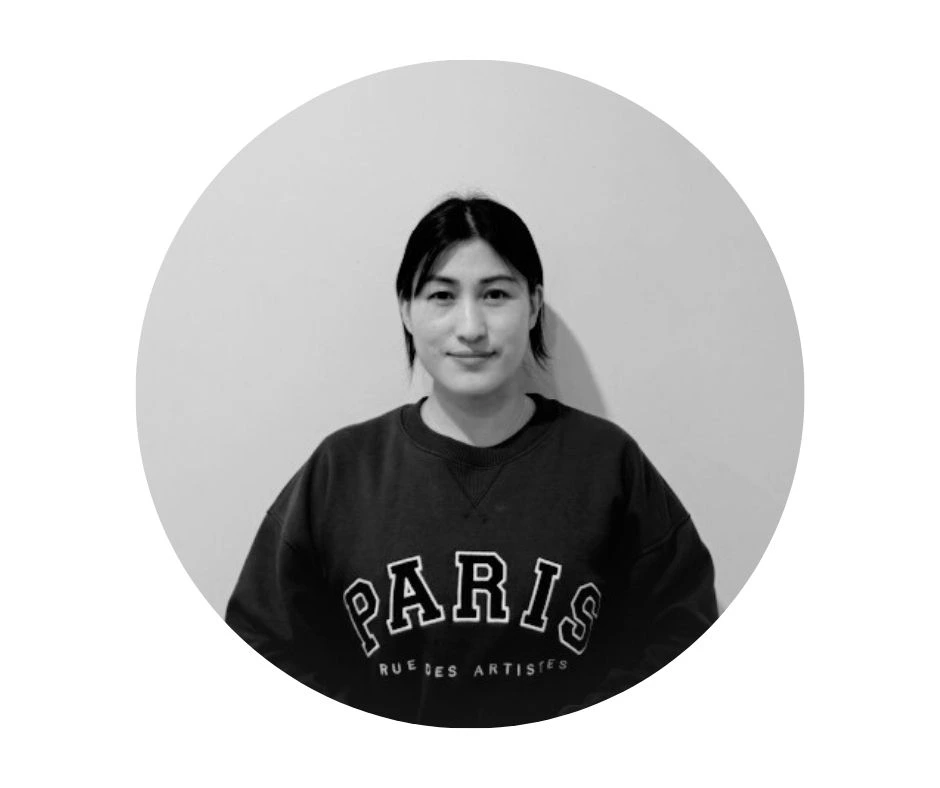 Meet our Babysitters A Cherished Cherubs babysitter with straight dark hair wearing a "PARIS" sweatshirt is centered against a plain, light-colored background in a circular frame.