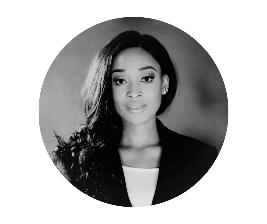 Meet our Babysitters Black and white portrait of a Cherished Cherubs Babysitter with long, wavy hair wearing a blazer and top, looking directly at the camera—a timeless image reminiscent of Cherished Cherubs photography against a plain background.