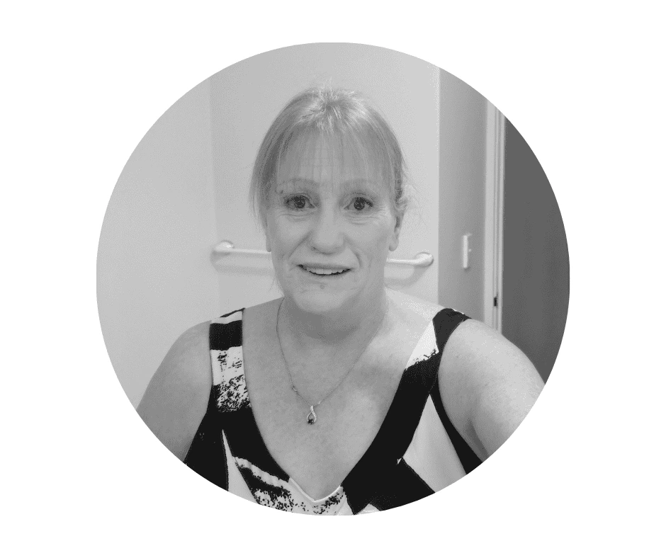 Meet our Babysitters A Cherished Cherubs Babysitter with light hair in a ponytail, wearing a patterned sleeveless top and necklace, smiles at the camera in a bathroom setting—capturing the warmth and joy of Cherished Cherubs.