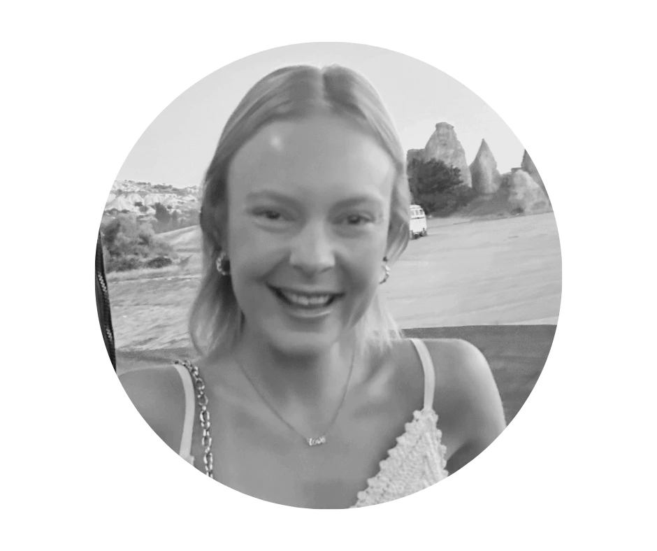 Meet our Babysitters A Cherished Cherubs Babysitter with shoulder-length hair smiles at the camera outdoors; Cherished Cherubs vibes radiate as rocky formations and a parked van are visible in the background.