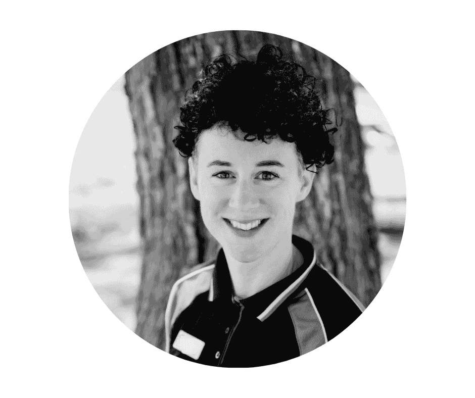 Meet our Babysitters A Cherished Cherubs Babysitter with short curly hair smiles at the camera in a collared shirt, standing outdoors before a tree—radiating the warmth and joy of Cherished Cherubs.