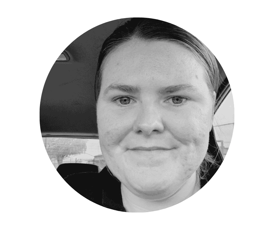 Meet our Babysitters A Cherished Cherubs Babysitter with straight hair pulled back, looking at the camera and smiling slightly, seated inside a car. The black and white image, framed in an oval, captures a moment reminiscent of cherished cherubs in its gentle simplicity.