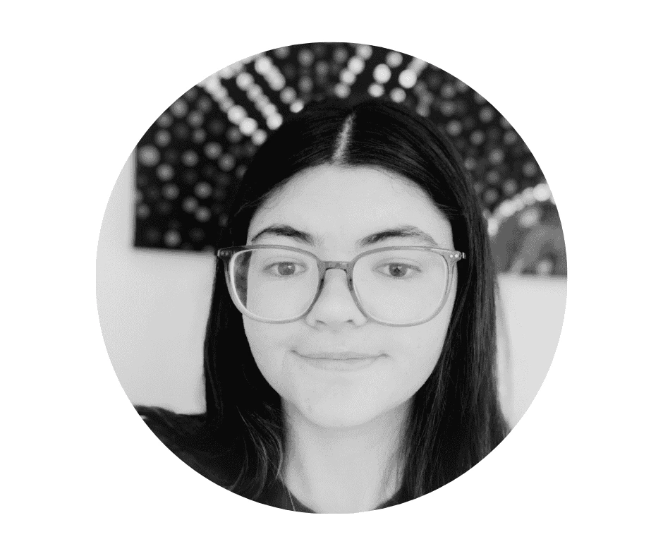 A Cherished Cherubs Babysitter with long dark hair and glasses looks at the camera and smiles slightly. The background features a circular pattern with dots, giving the image a timeless, classic feel—perfectly capturing the essence of Cherished Cherubs in black and white.
