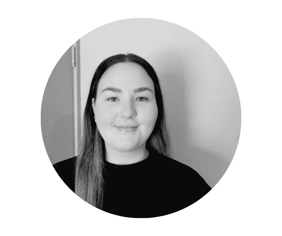 A Cherished Cherubs Babysitter with long straight hair, wearing a black top, smiles slightly while standing in front of a light-colored wall. This black and white photo, framed in an oval shape, beautifully captures the timeless charm of Cherished Cherubs.