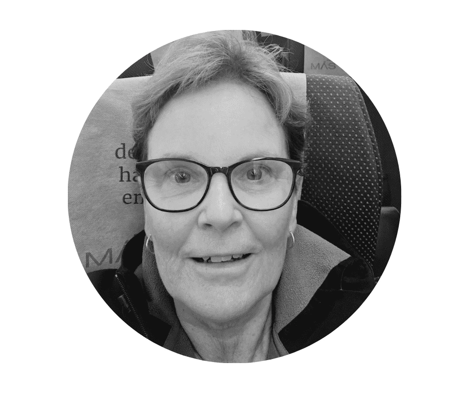 A Cherished Cherubs Babysitter with short hair and glasses smiles at the camera while sitting on a patterned seat, exuding the warmth and joy often seen in Cherished Cherubs.