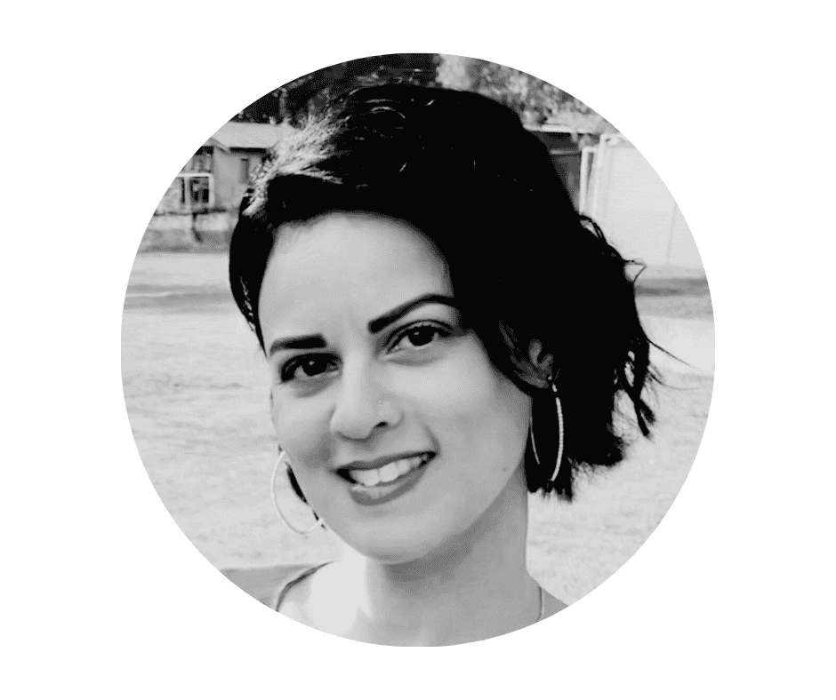 Black and white portrait of a Cherished Cherubs Babysitter with short dark hair, wearing hoop earrings, smiling outdoors with buildings blurred in the background—a cherished cherub moment captured in timeless elegance.