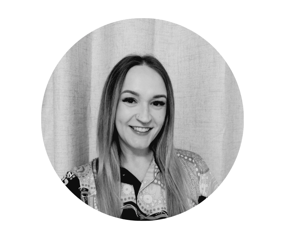 A Cherished Cherubs Babysitter with long straight hair smiles at the camera, standing before a light-colored curtain and wearing a patterned shirt. The black and white, circularly framed image radiates the warmth of Cherished Cherubs.